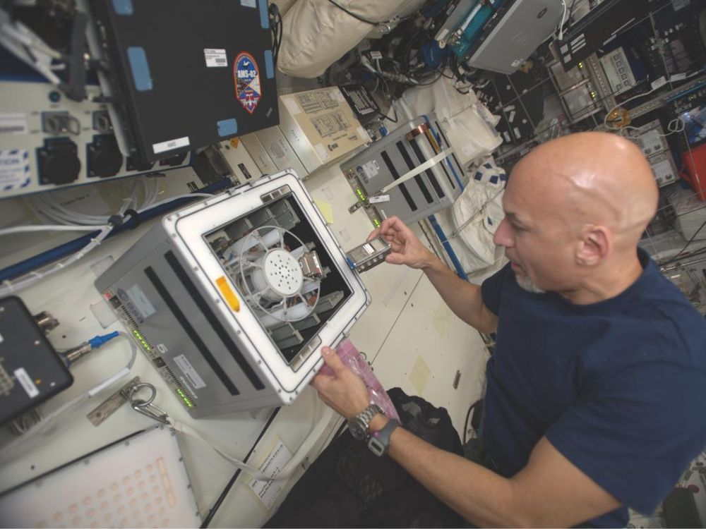 Astronaut in a blue t-shirt puts a small vial of bacteria and basalt in a centrifuge on the international space station