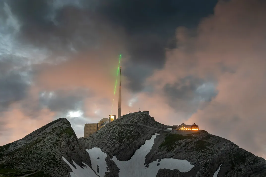 green laser shoots into sky beside tower on mountain