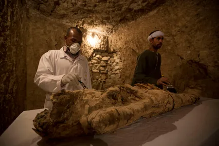 Egyptian excavation workers work on a mummy in a newly discovered tomb in Luxor, Egypt