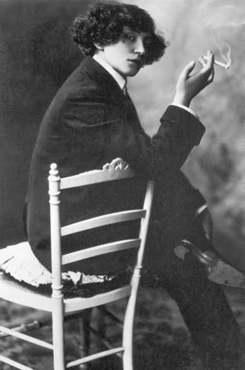 Colette, seated in a suit with a cigarette in her hand