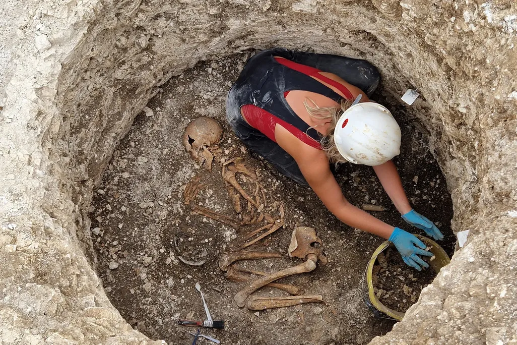 Researcher working in a hole dug into the ground next to a skeleton