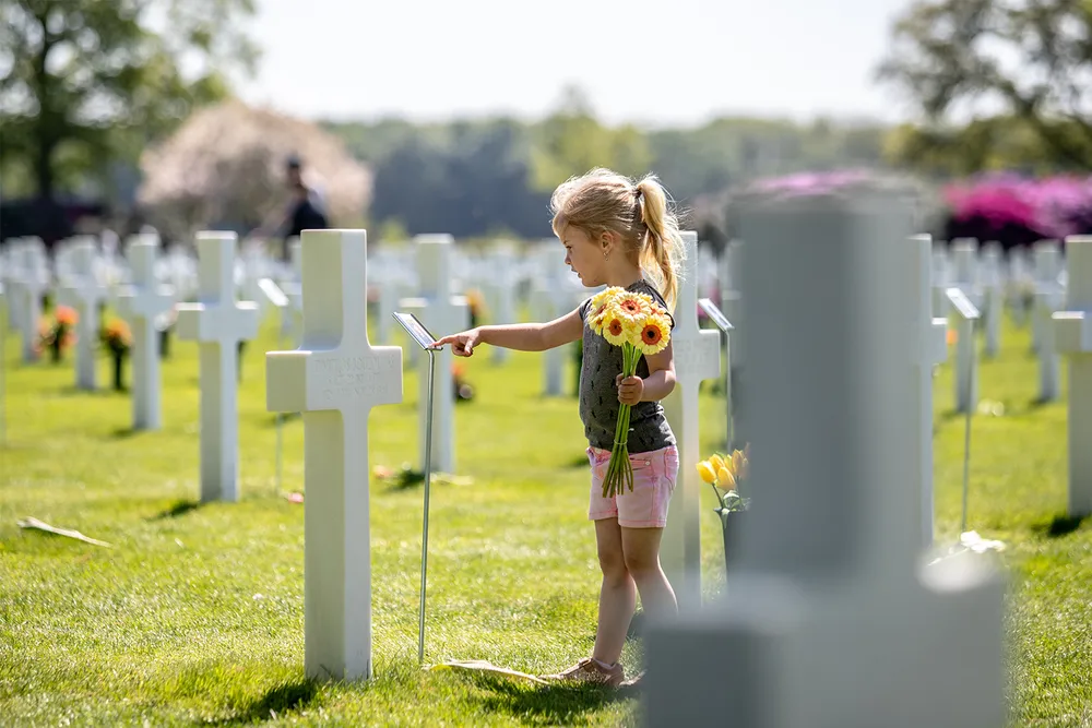 A child places flower on a grave at the Netherlands American Cemetery