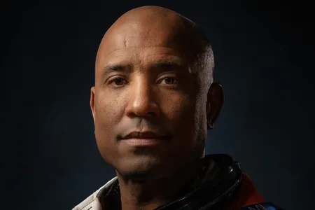 Dramatically-shot portrait of a Black male astronaut in an orange spacesuit.