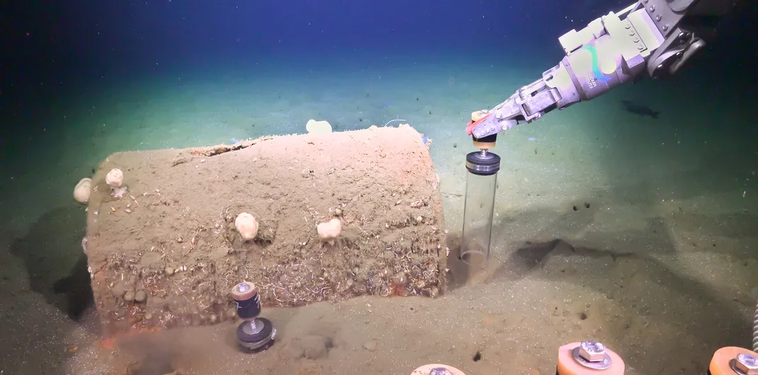 Robotic arm taking a sediment sample near a barrel