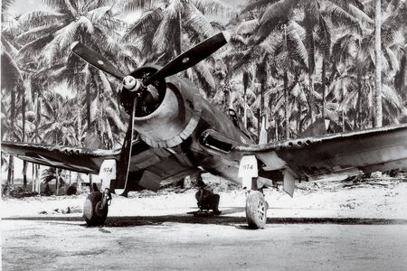 A VMF 222 Corsair catches some rays on Green Island while a ground crewman catches up on his reading.
