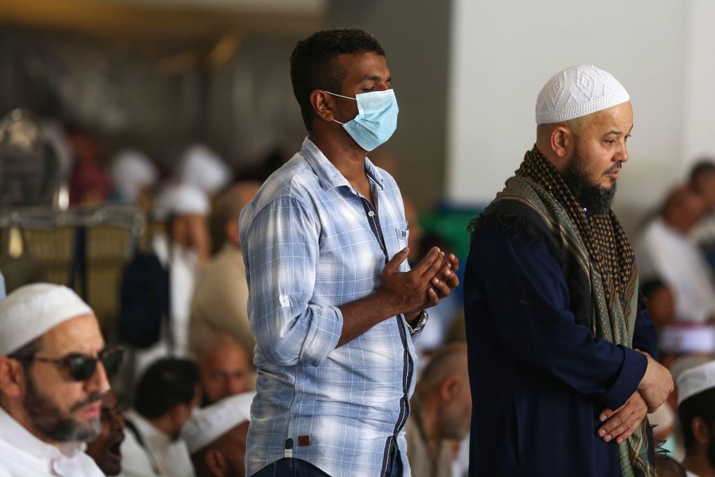 Muslim men pray at the Grand Mosque, one wearing a mask