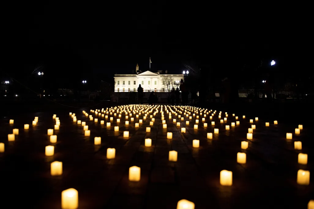 Electric candles on a lawn at night with the White House in the background