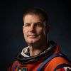 Dramatically-shot portrait of a white male astronaut in an orange spacesuit.