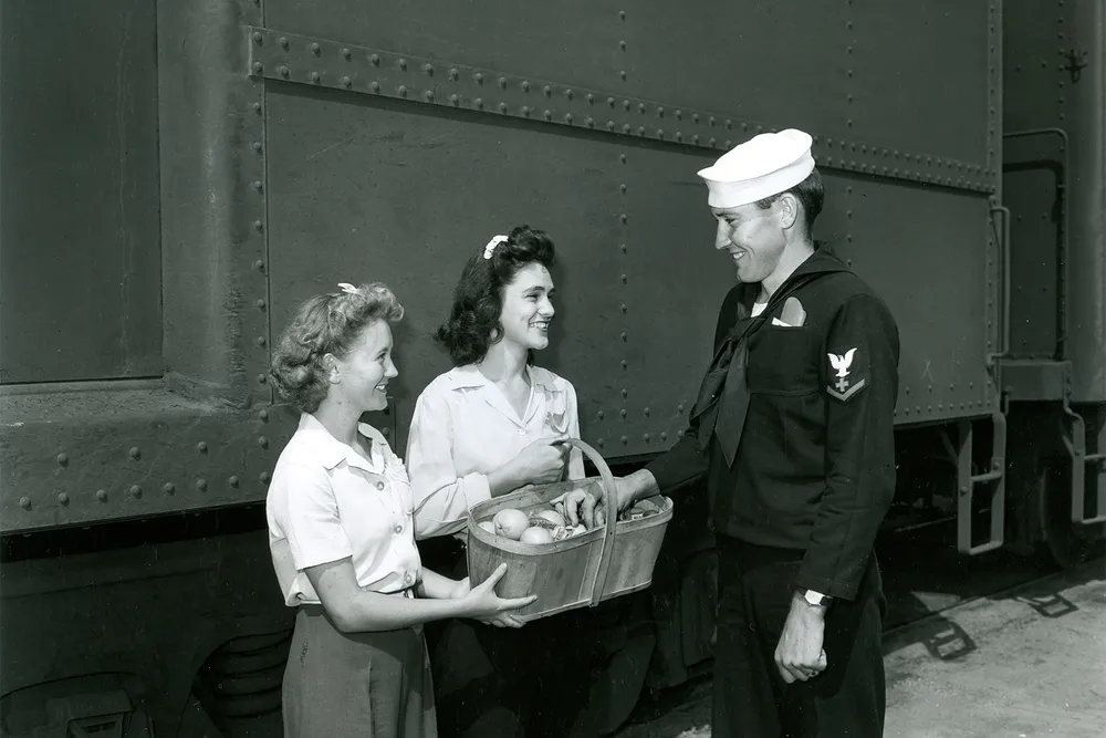 Two canteen volunteers offer a basket of food to a soldier