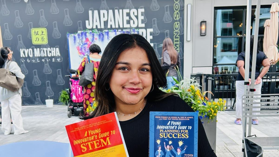 A teen with a black sweater on poses with two books