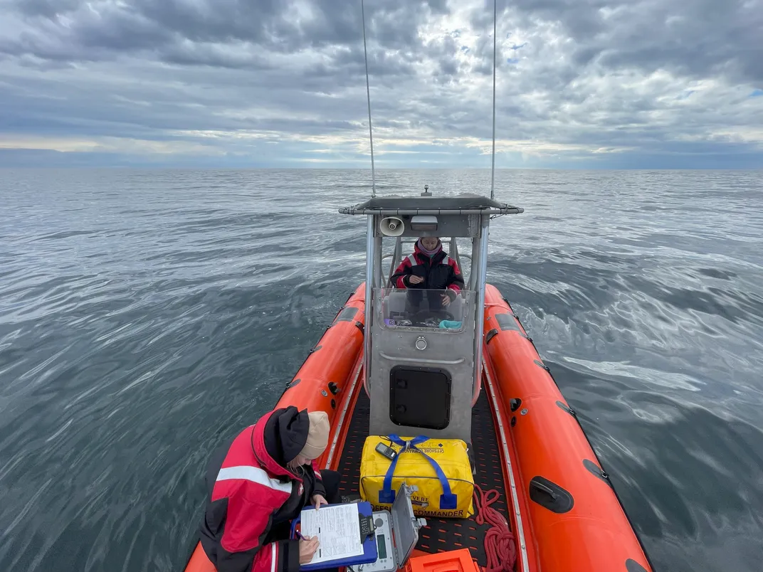 a scientist with a clipboard in a small orange boat as another drives