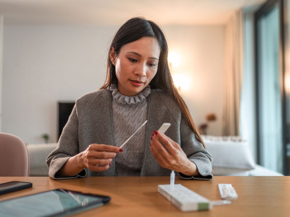 An asian woman takes an at home covid test and waits for the results at her table