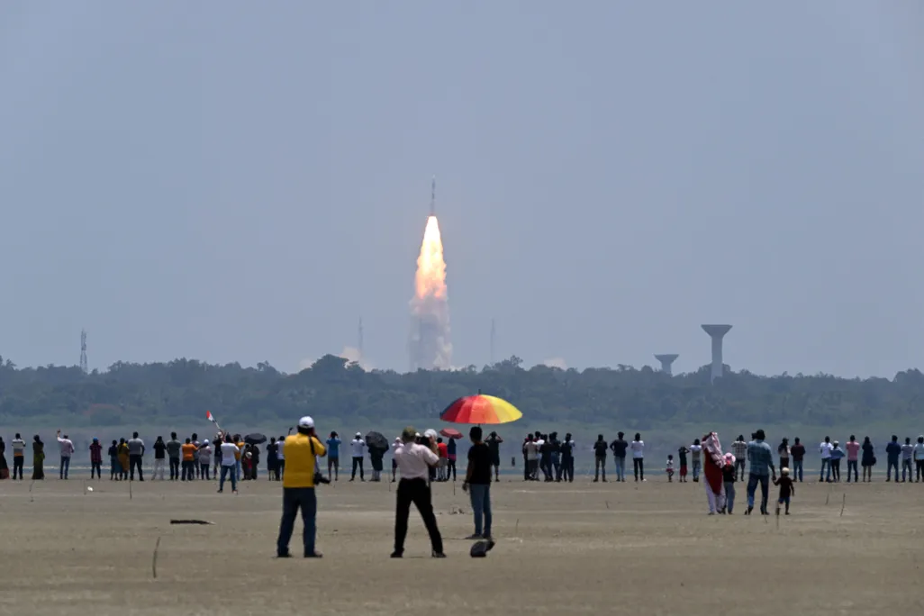 People stand and watch as a rocket takes off in the background
