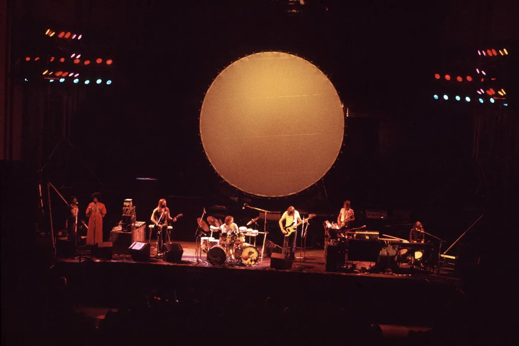 The band Pink Floyd plays on stage under an artistic rendering of a glowing moon