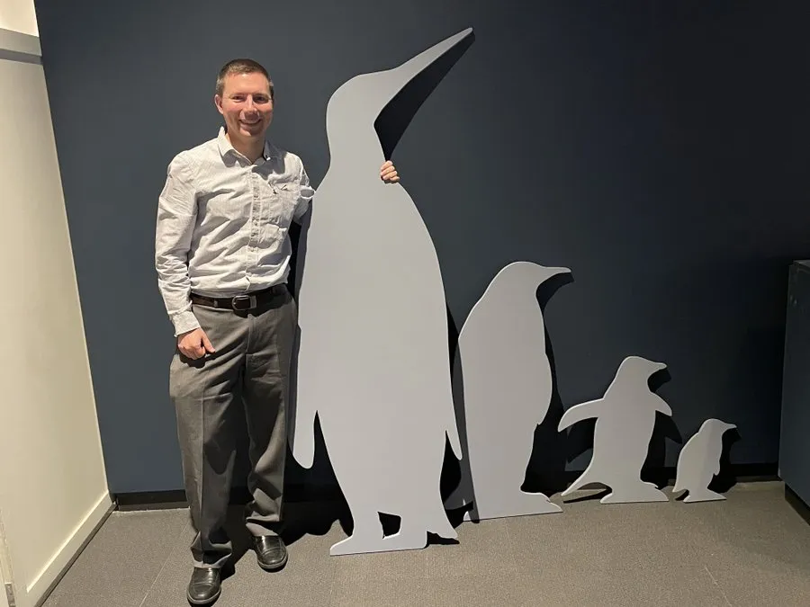 Researcher with penguin cutouts, one essentially as tall as him