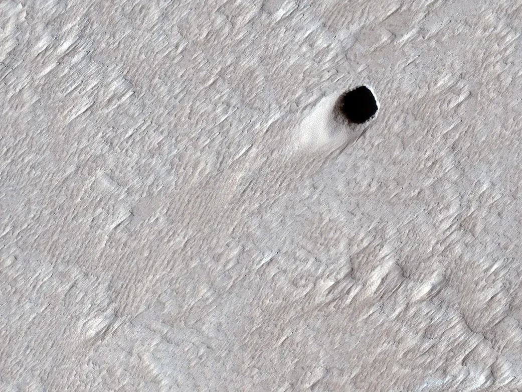 A pit crater, created by an empty lava tube, in Mars' Arsia Mons region. Captured by NASA's Mars Reconnaissance Orbiter in 2020.