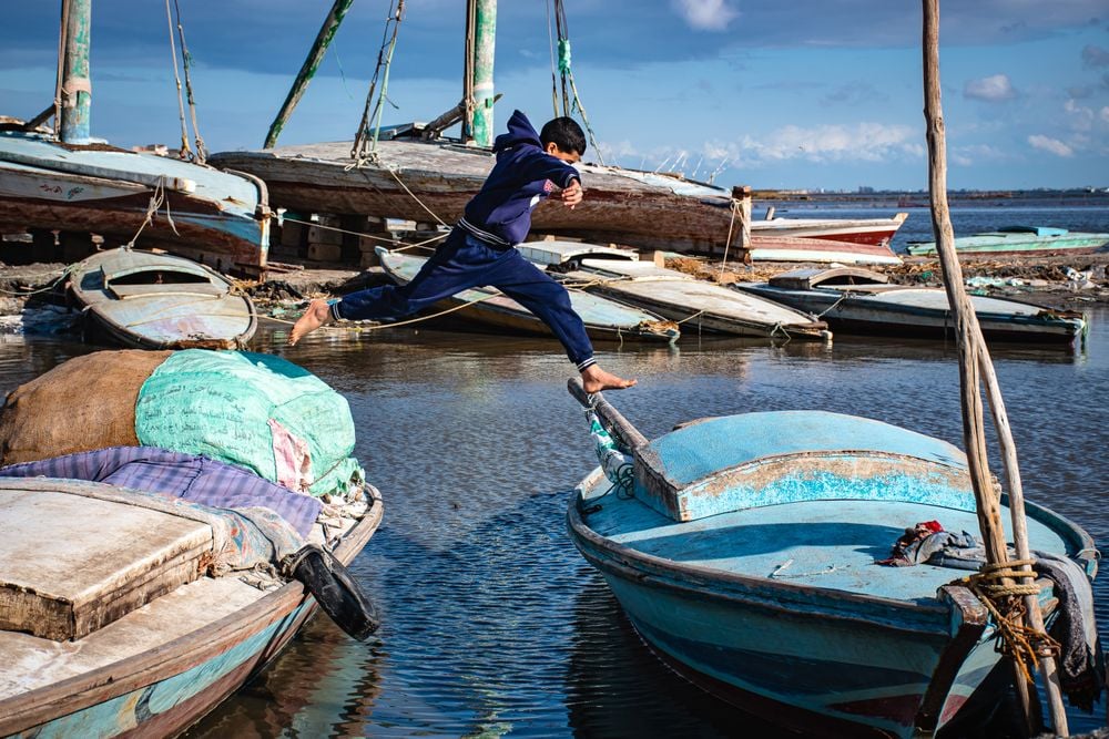Capturing the moment of the boy playing and jumping between the boats parked in the lake inside one of the villages of the Egyptian countryside.