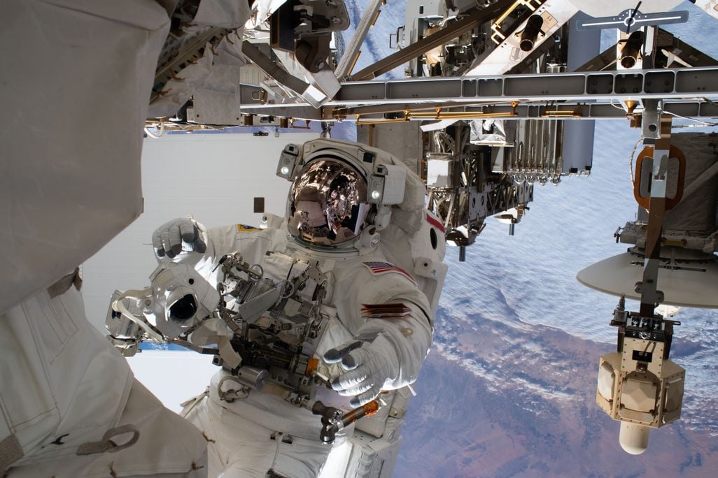 An astronaut tethered to the outside of the International Space Station, with a view of Earth behind.