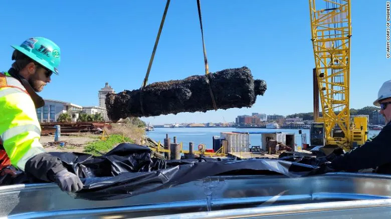Worker in yellow safety vest working machinery that lifts rusted cannon from water