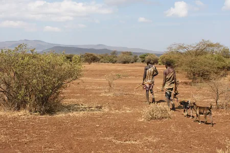 Two Hadza men in Tanzania carry bows and their catch.