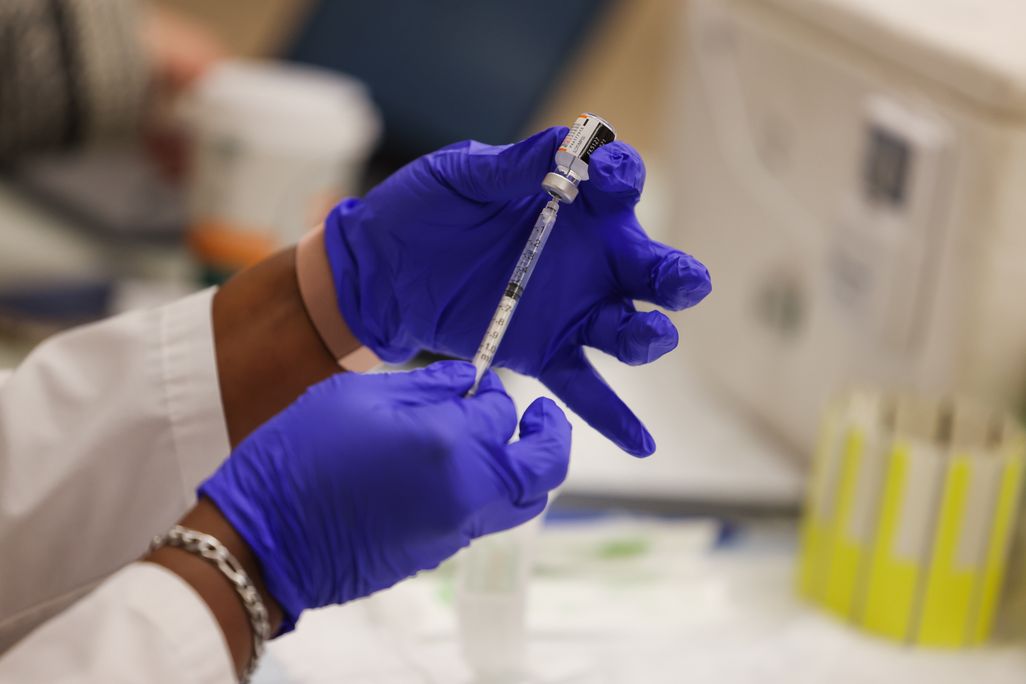 A close-up of gloved hands filling a syringe with a Covid-19 booster shot