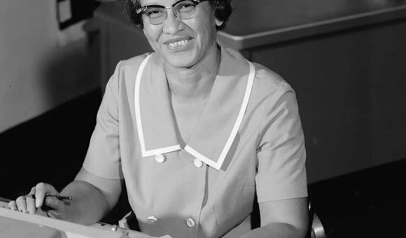A black and white photo of Katherine Johnson sitting at a desk in front of a typewriter and open notebook.