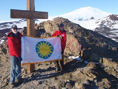Kristina Johnson and Wayne Clough hoist the Smithsonian flag atop Observation Point—a site memorializing explorers who have died at the South Pole.