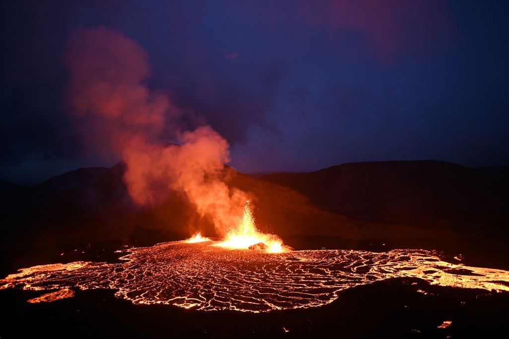 Lava and smoke rise from the volcano in the dark, surrounded by a ring of glowing lava