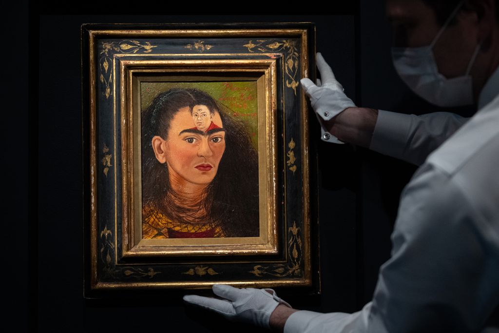 A self portrait of Kahlo from the neck up, with a dark cloud of hair, a deep red shirt and lips and three tiny pearl tears; a small portrait of Diego with three eyes rests on her browbone