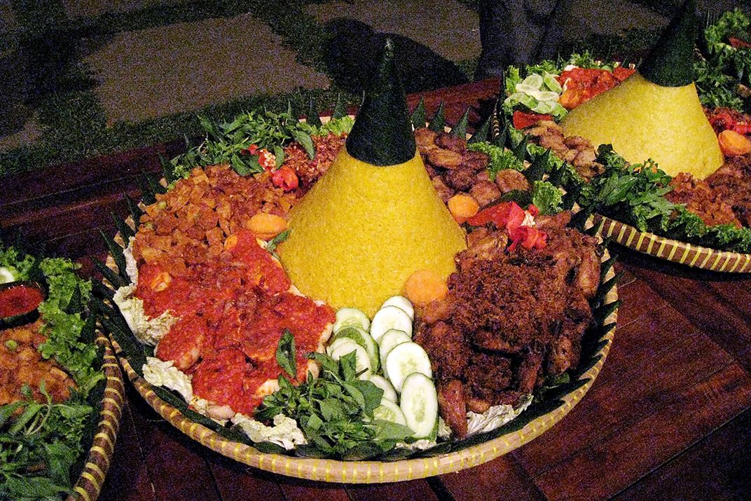 Three woven food platters, each with a central mound of  yellow rice surrounded  by bright red and brown meats and greens.