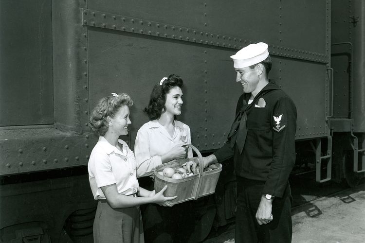 Two canteen volunteers offer a basket of food to a soldier
