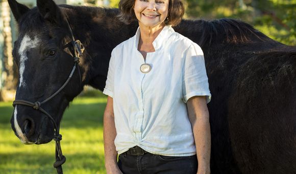 Image shows a woman wearing a white shirt standing with and holding the reins of a horse