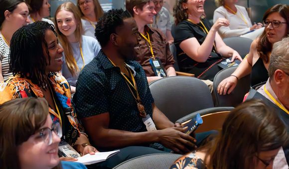 A group of men and women are in an audience turning and talking to each other with smiles