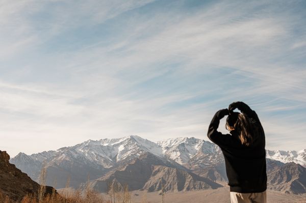 A girl making a heart with her arms while looking at the mountains. thumbnail