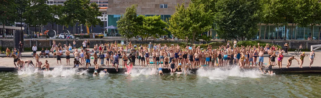 a long line of people jumps from the shore into the harbor in Rotterdam