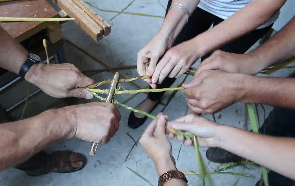 four pairs of hands spin cattail fibers through a replica of a Stone Age perforated baton