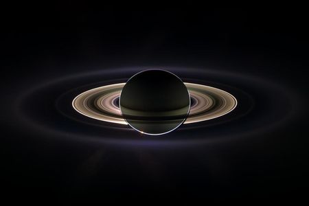 Saturn and its rings backlit by the sun, which is blocked by the planet in this view. Encircling the planet and inner rings is the much more extended E-ring.