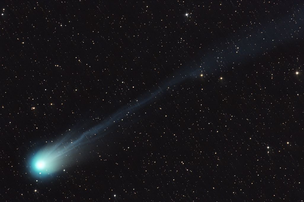 a comet streaks diagonally across the frame, with its bright green nucleus at the bottom left