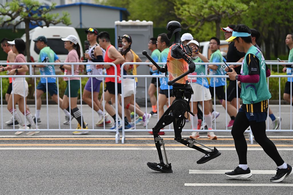 The winning humanoid racing alongside human runners with a technician close behind.
