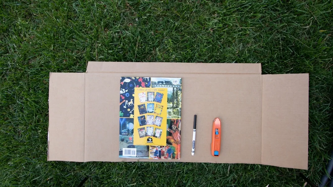 Book and marker on top of cardboard laying on grass.