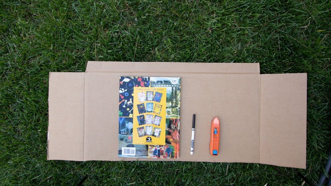 Book and marker on top of cardboard laying on grass.