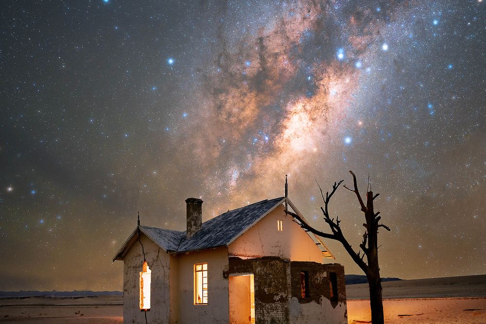 The Milky Way seen from Earth with an abandoned desert house and bare tree in the foreground