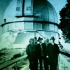 A black-and-white historical photograph from circa 1931 shows Albert Einstein with Edwin Hubble and other astronomers standing on a walkway in front of the large dome of the Mount Wilson Observatory.