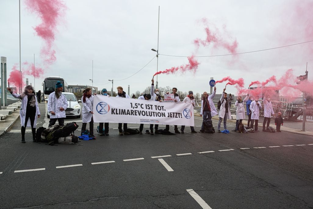 Protesters in Berlin wear white lab coats and hold a sign