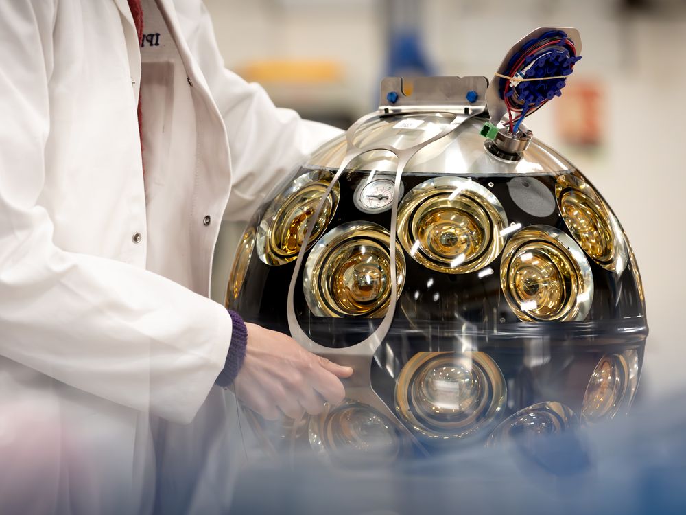 a scientist's hands hold onto a large metal sphere with many dials