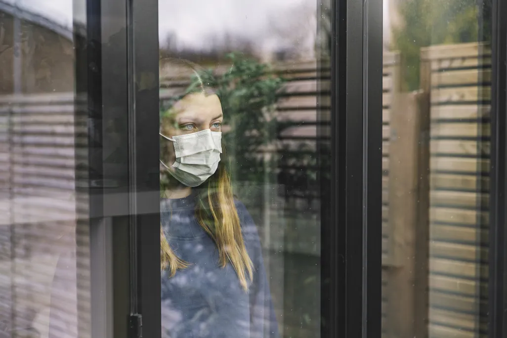 Woman wearing mask stares out a window
