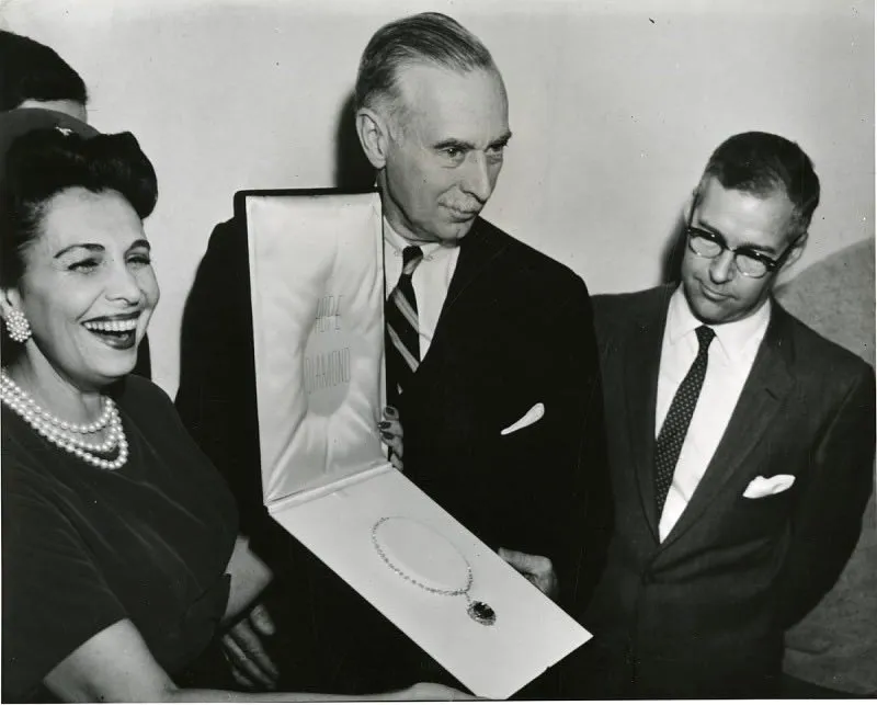 Two men and a woman stand together holding a case with a large diamond inside in this black and white image