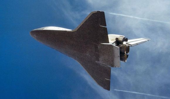 Underside view of space shuttle in flight with blue sky background.