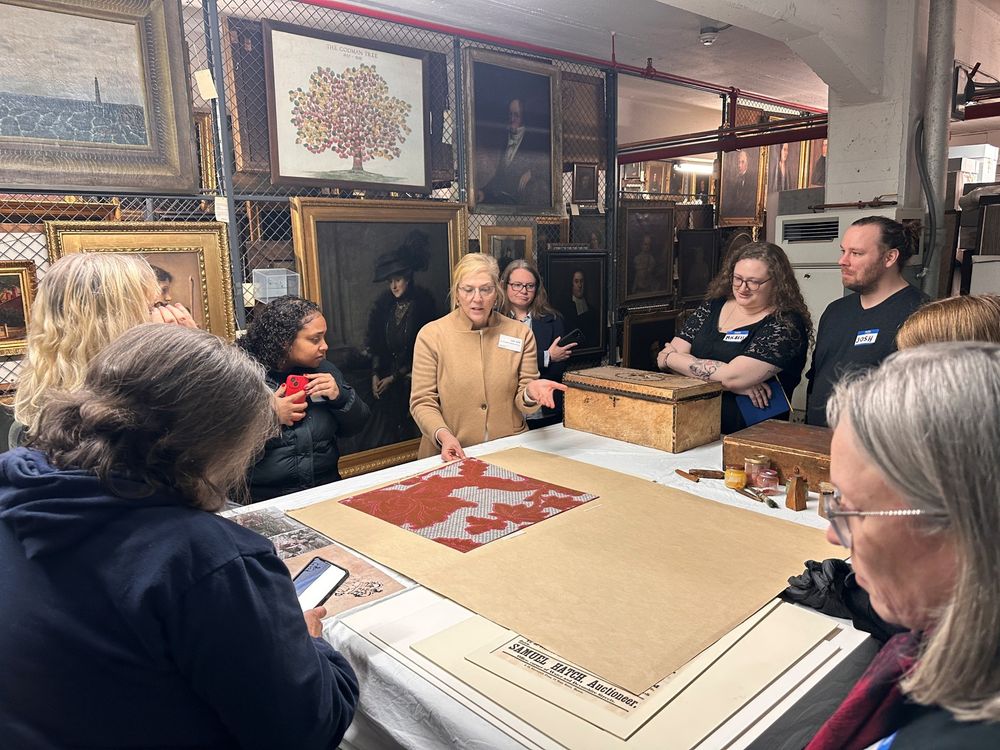 A group of workshop participants standing around a table listening to a curator discuss an artifact within Historic New England’s collection.