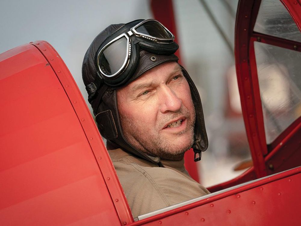 Andrew King wearing a vintage helmet and goggles in red cockpit